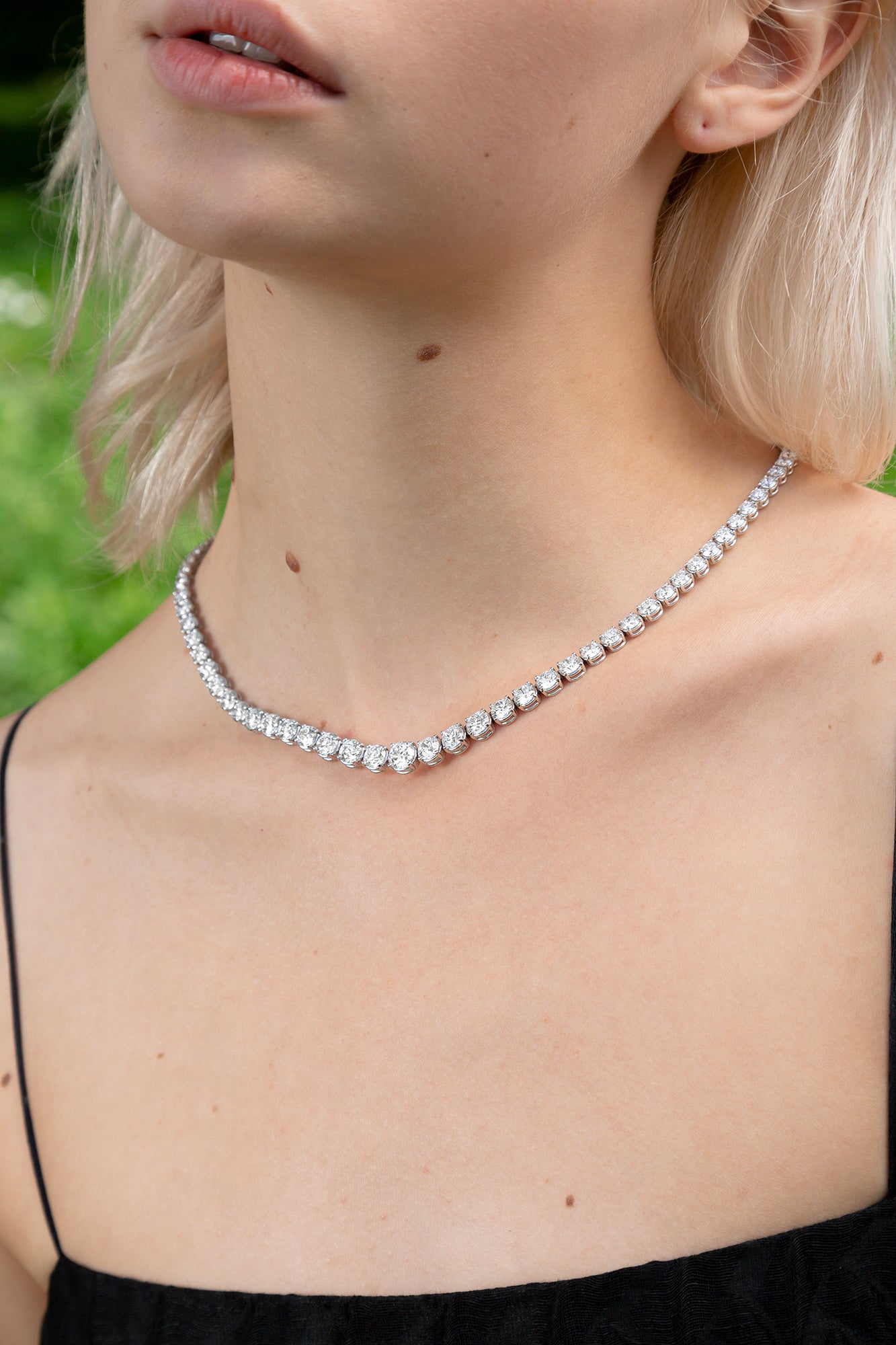 A model wears the Collier Rivière Tennis Necklace as an addition to a springy cocktail look. This 25ct graduated diamond tennis necklace features flawless round brilliants in a four prong solitaire setting. D-color, IF/VVS diamonds crescendo toward a center diamond of 1ct. The length of this striking piece is 16 inches (40cm).