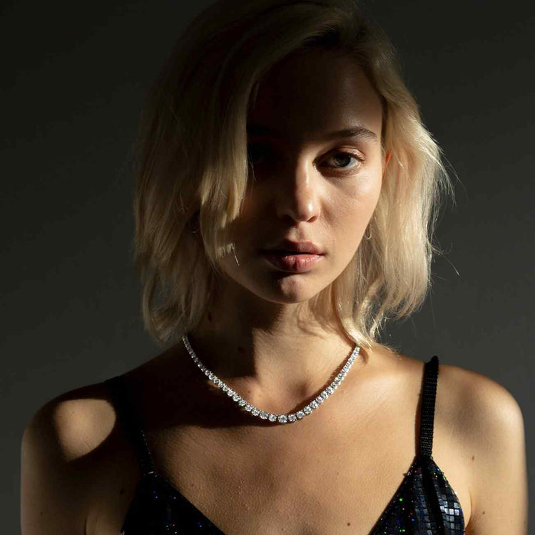 A model wears the Collier Rivière Tennis Necklace. This 25ct graduated diamond tennis necklace features flawless round brilliants in a four prong solitaire setting. D-color, IF/VVS diamonds crescendo toward a center diamond of 1ct. The length of this striking piece is 16 inches (40cm).