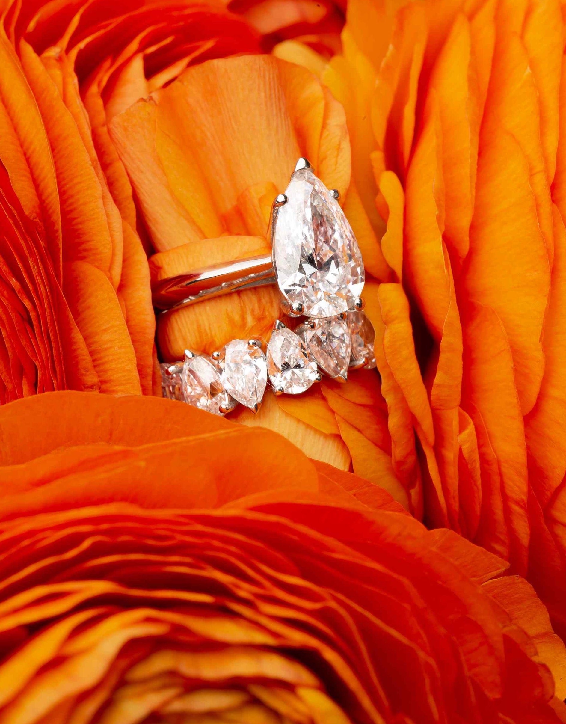 A 3.5 carat Pear diamond solitaire radiates in a knife-edge setting of Palladium & 18K White Gold, sitting between the petals of a deeply vibrant orange flower. The magic of the pear diamond is replicated with a matching 5tcw Sans Cesse Pear ring in White Gold.