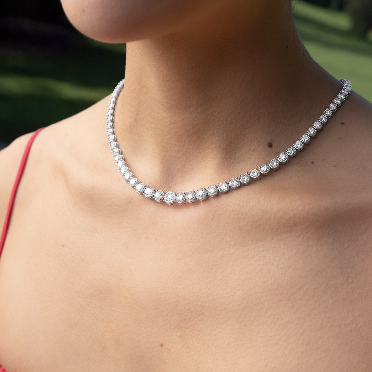 A model wears the Collier Rivière Tennis Necklace as an addition to a springy cocktail look. This 25ct graduated diamond tennis necklace features flawless round brilliants in a four prong solitaire setting. D-color, IF/VVS diamonds crescendo toward a center diamond of 1ct. The length of this striking piece is 16 inches (40cm).