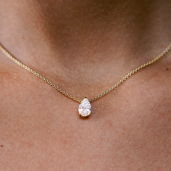 A model wears the Île Pear Necklace with a Yellow Gold setting and chain. A solitaire pear diamond is centered between the collarbone on an 18k gold chain. The length of this necklace is 16" (40cm). Please get in touch if you would like a different chain length. Shape, color, and size of this pear diamond necklace are fully customizable as well.