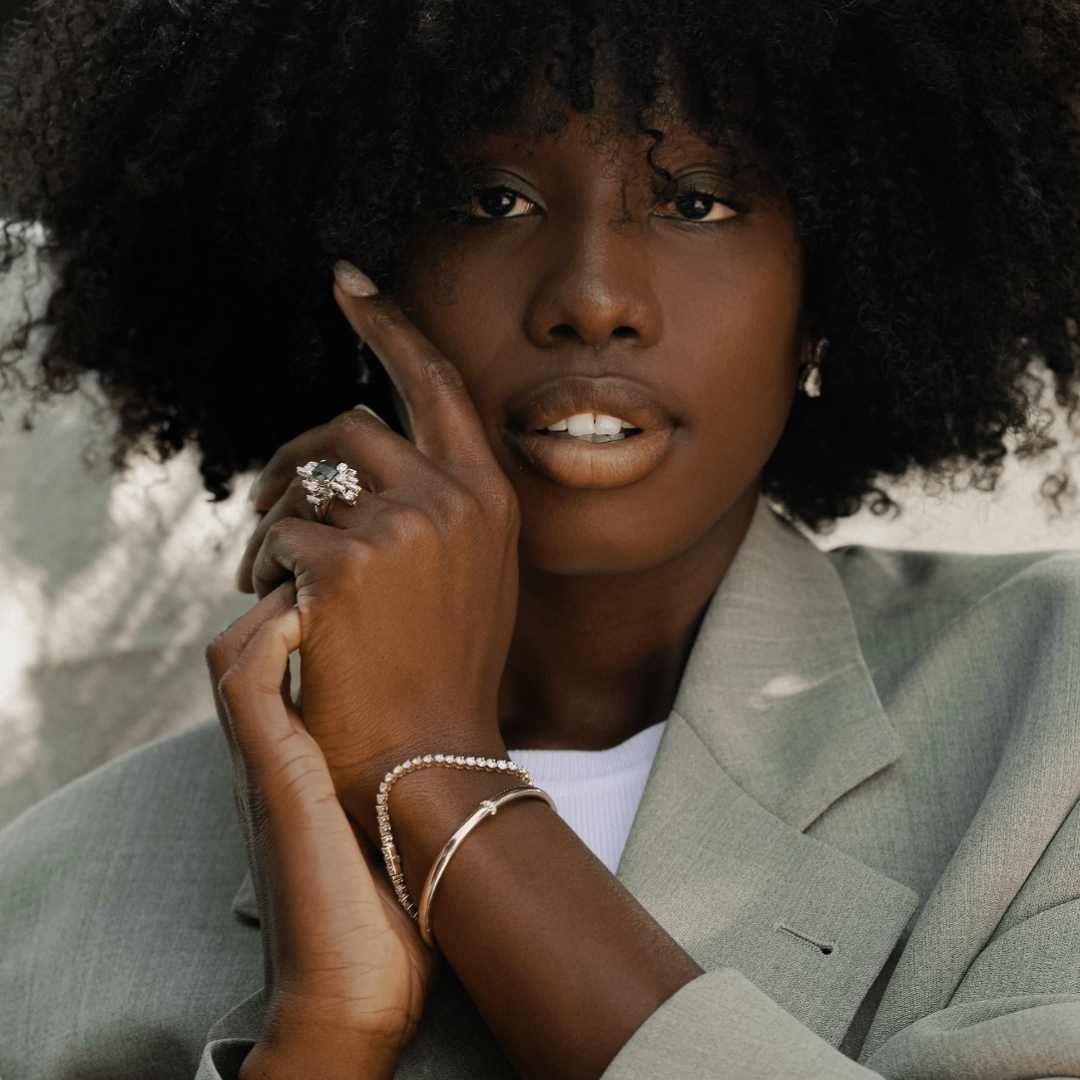 A model wears the Dalliance Gold Bangle paired with the Bracelet George Rivière Tennis Bracelet for the perfect bracelet stack. The diamonds in the Tennis Bracelet pair perfectly with the thin strip of diamonds on the gold bangle. Also shown here with other High Jewelry pieces - the Nina Ring and the Bisous de Poires pear diamond earrings.