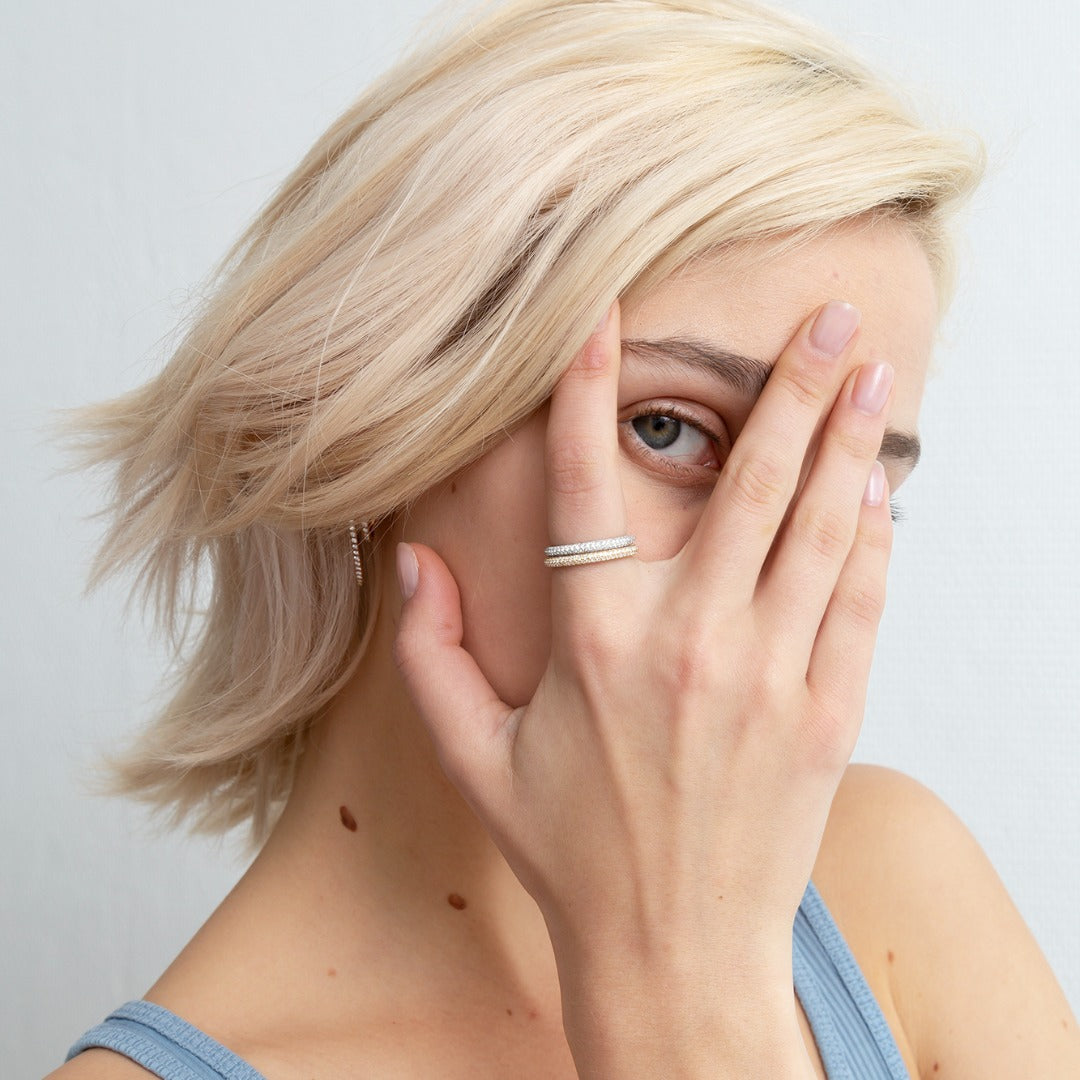 A model wears two Dalliance Pavé rings - the top in 18k White Gold, and stacked below, in 18K Yelloow Gold. Each is a three-row diamond pavé ring that features D color, IF/VVS clarity round brilliants meticulously hand-placed in 4.5 grams of recycled 18k gold.