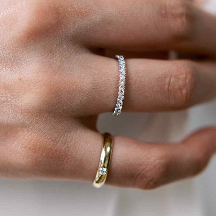 A model wears the Éternité ring (in White Gold) on her ring finger paired with the Talia Pinky Ring. D color, IF/VVS clarity round brilliants held in 2.55 grams of recycled 18k gold for a timeless pavé diamond eternity band totaling ~0.8ct.