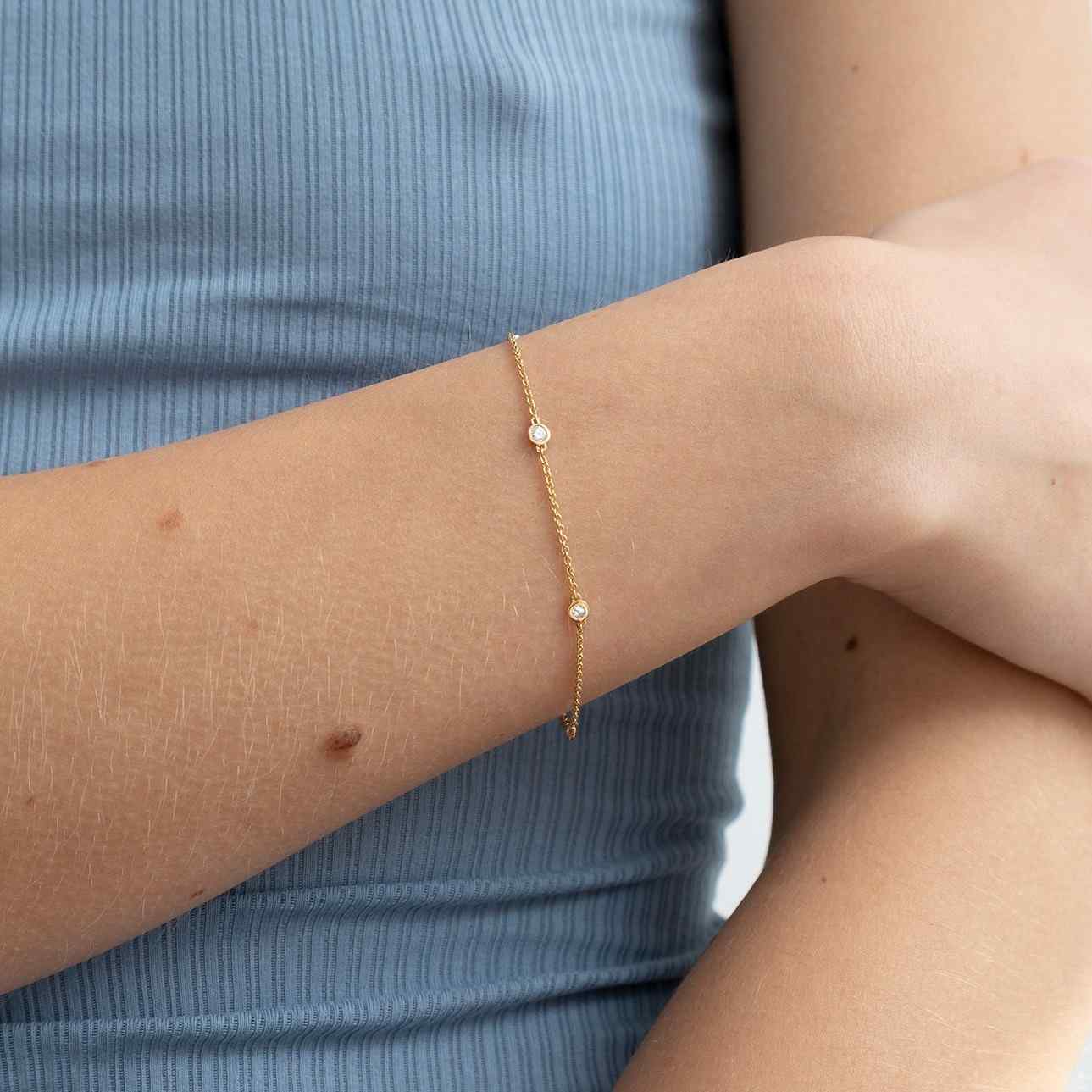 A model wears this delicate bracelet, which features five bezel-set round brilliants totaling 0.25ct. The diamonds sit in a gold chain of recycled 18K gold. This bracelet can be adjusted to two different lengths, 6.3" (16 cm) and 6.7" (17 cm).