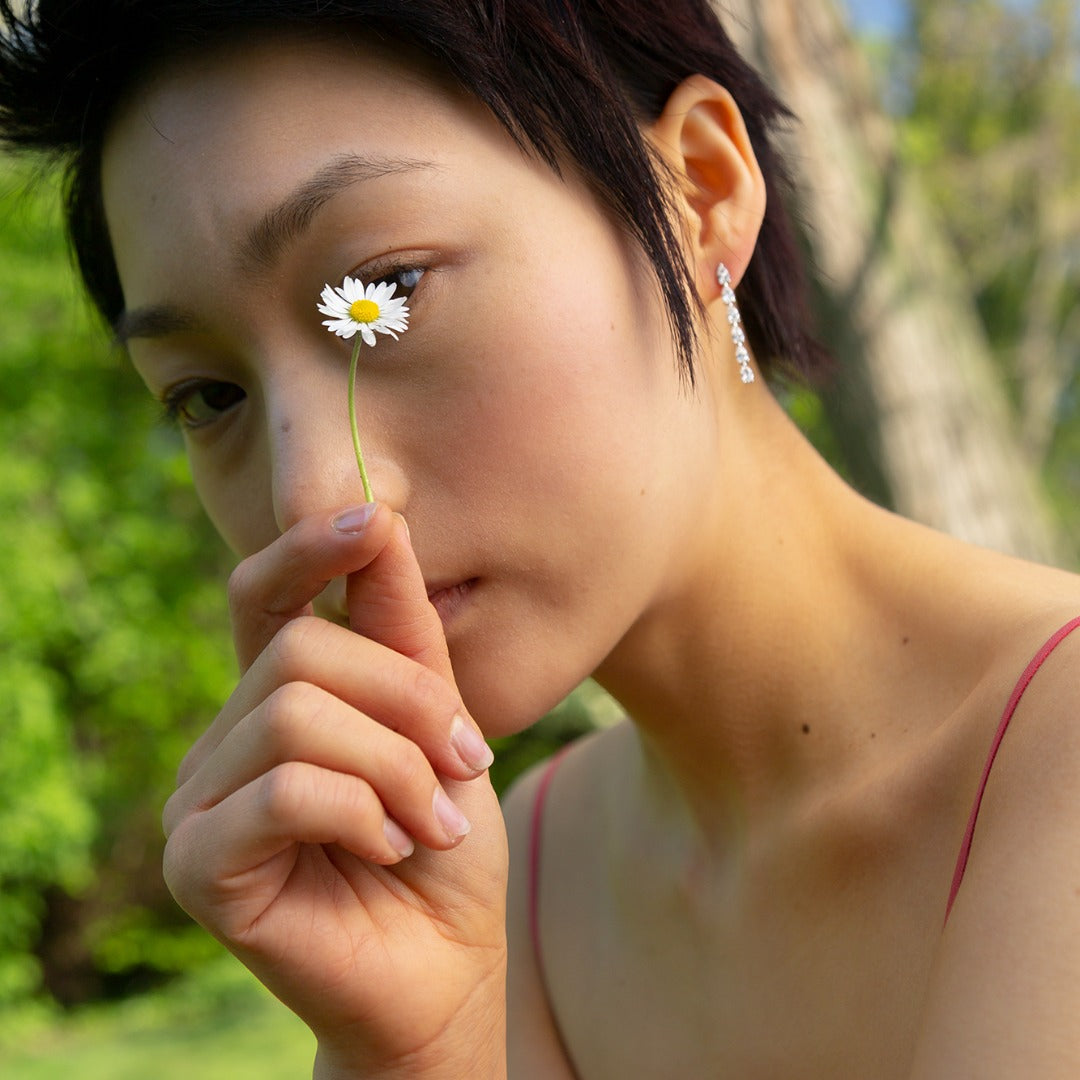 A model wears the striking Île Column Grande Earrings - which shine on their own. Hand-cast from 3.6 grams of recycled 18k gold, these pear diamond earrings feature six pristine tear drops floating in an architectural column. The pair of earrings is 2 total carat weight. The shape and size is fully customizable.