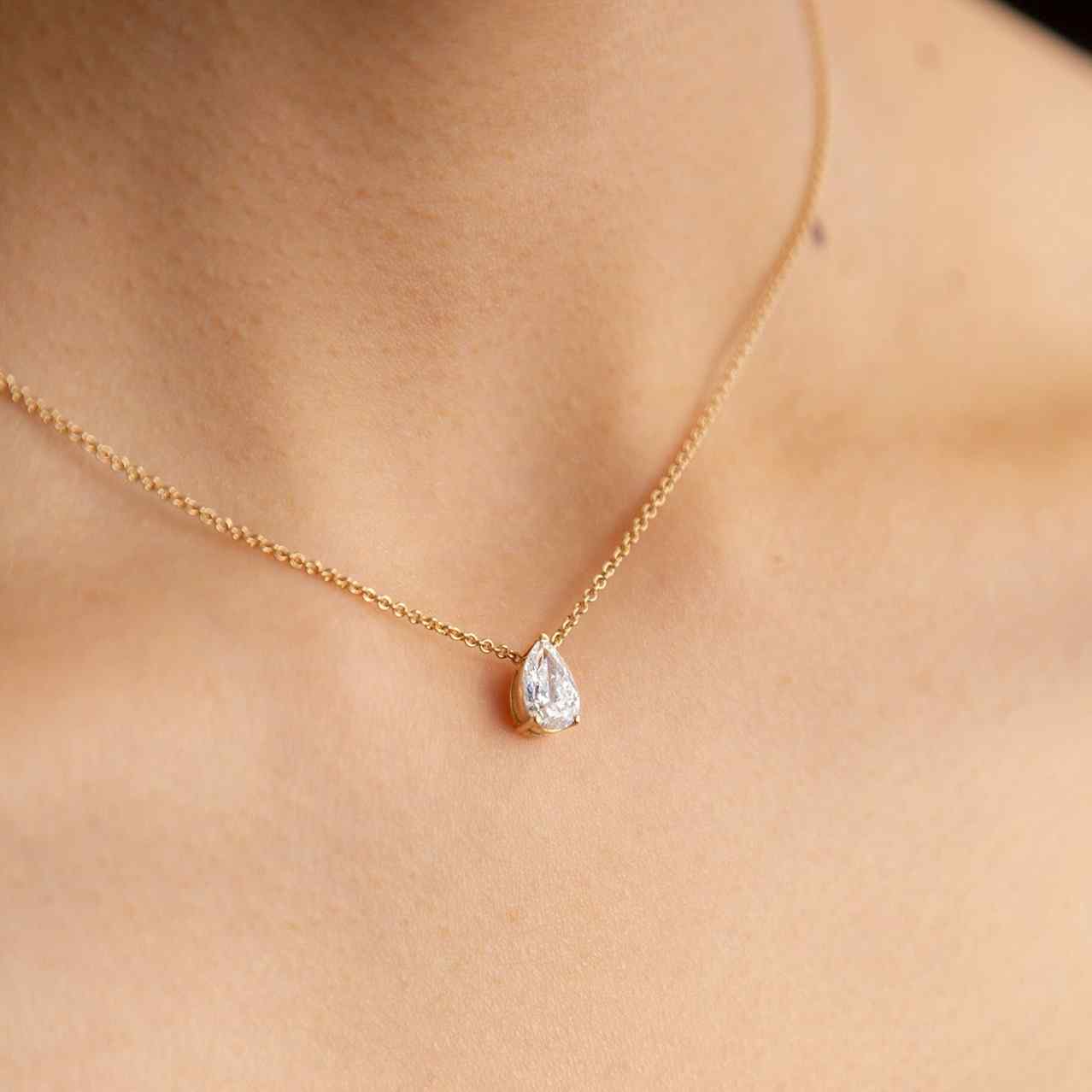 A model wears the Île Pear Necklace with a Yellow Gold setting and chain. A solitaire pear diamond is centered between the collarbone on an 18k gold chain. The length of this necklace is 16" (40cm). Please get in touch if you would like a different chain length. Shape, color, and size of this pear diamond necklace are fully customizable as well.