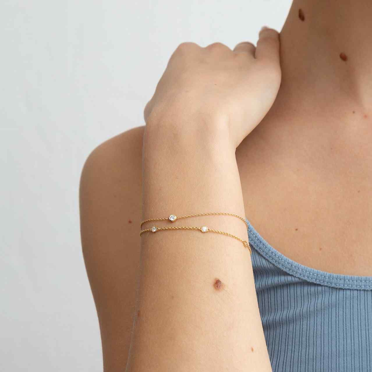 A model wears this delicate bracelet - which features a solitaire 0.1 carat round brilliant bezel set in 18k recycled gold. This bracelet can be adjusted to two different lengths, 6.3" (16 cm) and 6.7" (17 cm). Shown here in Yellow Gold and paired with the Étoiles Bracelet for a delicate bracelet stack.