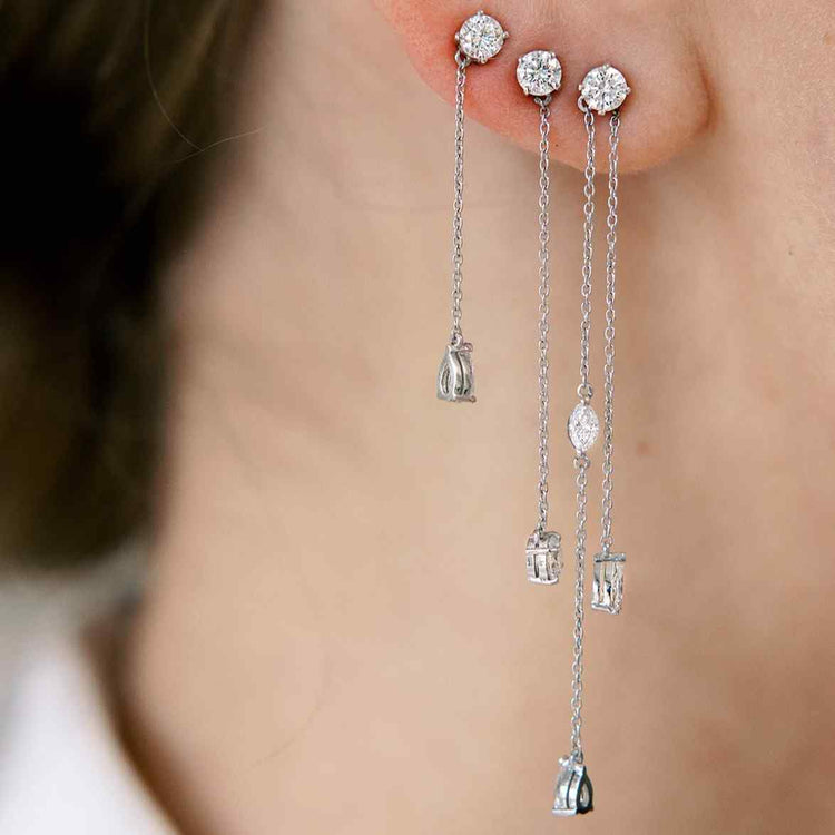 A model wears a stack of the Lariat earrings. The first hole has the Lariat Trois earrings with a custom jacket (or additional chain with a diamond) that attachs through the stud. The second hole features a custom Lariat Deux with a longer chain, and the Lariat Deux Earring is in the model's third hole. The combination of the three earrings creates the appearance of dancing diamonds - perfect for an elevated evening or wedding look.