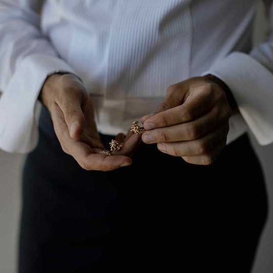A model holds the Boutons de Manchette, or Cufflinks, which feature 23 grams of solid 18K Yellow Gold, hand-cast to emulate the birch trees of Belgium. Perfect as a men's wedding gift.