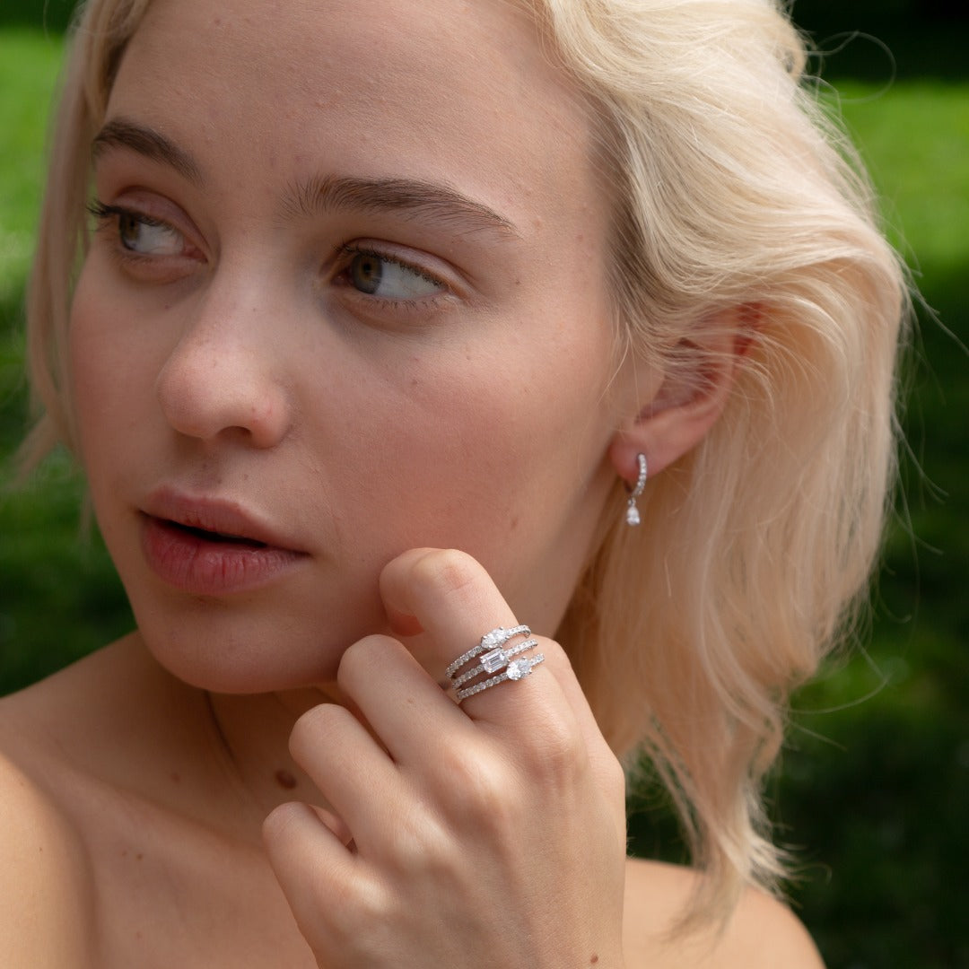 A model wears the Paire de Poires drop earrings with the Trois Pierres ring set. The Paire de Poires earrings feature a 0.15 carat D color, IF/VVS clarity pear diamond that dances at the bottom of an 8mm drop huggie. Sold as a pair, totaling 0.52 carat and 2.36 grams of 18k recycled gold.