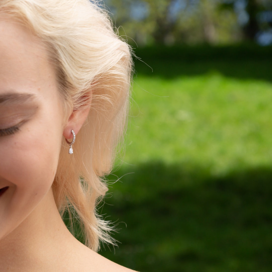 A model wears the Paire de Poires drop earrings - a 0.15 carat D color, IF/VVS clarity pear diamond that dances at the bottom of an 8mm drop huggie. Sold as a pair, totaling 0.52 carat and 2.36 grams of 18k recycled gold.