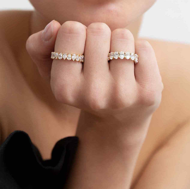 A model wears the Sans Cesse Oval Eternity on her ring finger - 18K Yellow Gold and 5 total carat weight. Paired with the San Cesse Pear Eternity (2.5tcw, also Yellow Gold) for a warm gold set. The Gold is 18K Recycled and diamonds are D Color, IF/VVS clarity - all lab-grown.