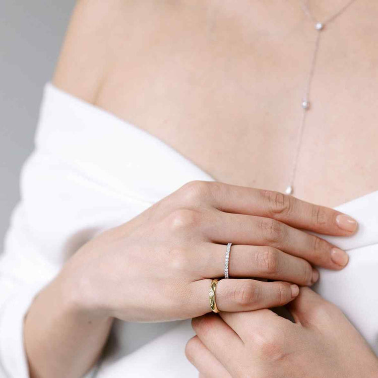 A model wears the Talia Pinky Ring - 3.3 grams of glimmering 18k recycled gold centered around a round brilliant of 0.1ct. Yellow Gold shown here. Paired with the Éternité diamond band and Lariat Necklace.