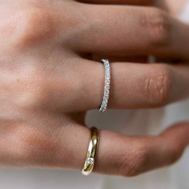 A model wears the Talia Pinky Ring - 3.3 grams of glimmering 18k recycled gold centered around a round brilliant of 0.1ct. Yellow Gold shown here. Paired with the Éternité diamond band as the perfect everyday jewelry.
