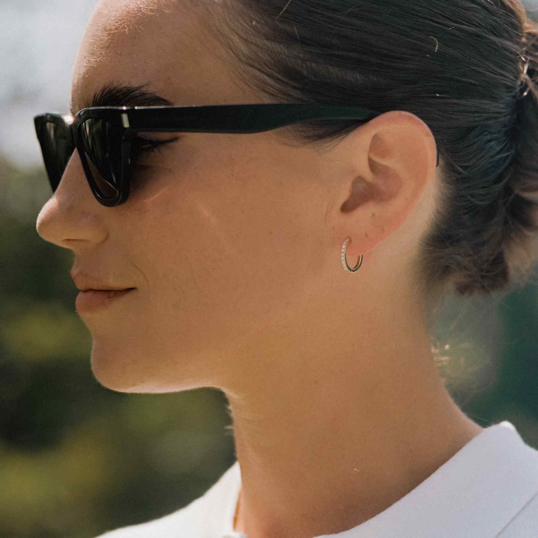 A model wears the Toujours earrings - a classic 12mm diamond hoop featuring 22 D color, IF/VVS clarity round brilliants in 18k gold. Sold as a pair.