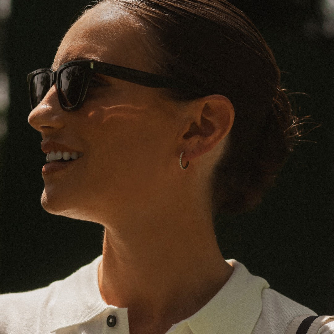 A model wears the Toujours earrings - a classic 12mm diamond hoop featuring 22 D color, IF/VVS clarity round brilliants in 18k gold. Sold as a pair.