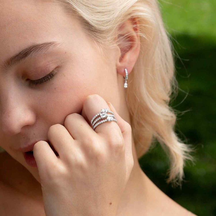 A model wears the Trois Pierres set - three rings of varying diamond shapes paired together. Diamond center shapes from top ring to bottom: marquise, emerald, and oval, with pavé diamonds around the entire band. The center diamonds is fully customizable to any shape and any pairing.